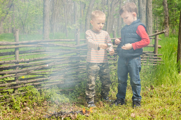 Naklejka na ściany i meble Two young boys play alongside a smoking fire
