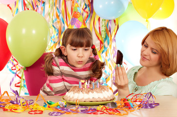 Mother taking picture while daughter blowing the candles on the