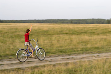 boy on bike rides along the road in the field.
