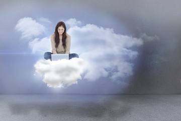 Composite image of brunette sitting on cloud using laptop