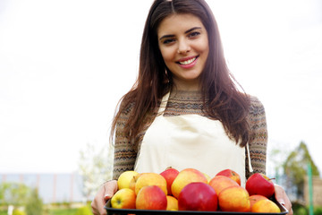 Portrait of a smiling woman holding basket with apples in garden