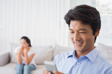 Man sending a text while girlfriend watches from couch