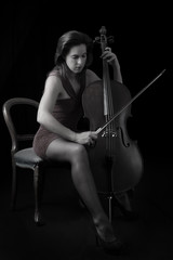 Beautiful brunette playing cello with selective light in red dre