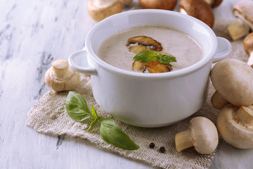 Mushroom soup in white pot, on napkin, on wooden background