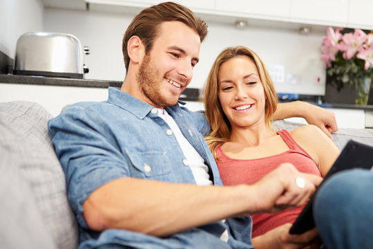 Young Couple Sitting On Sofa Using Digital Tablet