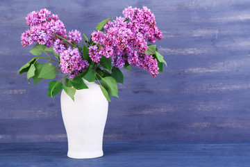 Beautiful lilac flowers in vase, on color wooden background