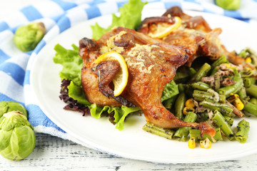 Roasted quails with vegetables on plate, on wooden background