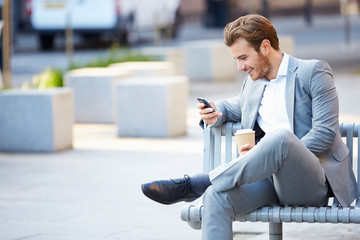 Businessman On Park Bench With Coffee Using Mobile Phone - Powered by Adobe