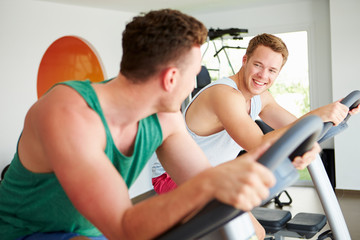 Fototapeta premium Two Young Men Training In Gym On Cycling Machines Together