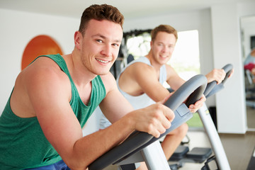 Obraz premium Two Young Men Training In Gym On Cycling Machines Together