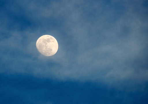 Shiny moon in cloudy skies before dusk