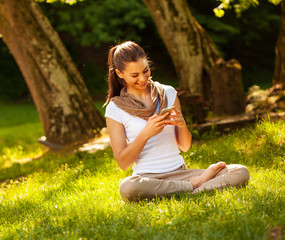 Attractive female typing sms message while sitting on grass.