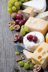 assortment of cheeses, grapes and walnuts on a wooden background