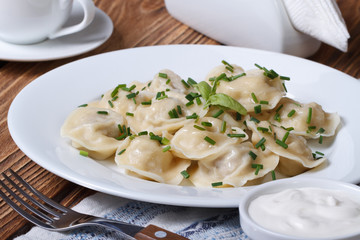 dumplings with sour cream on a white plate with onion chives