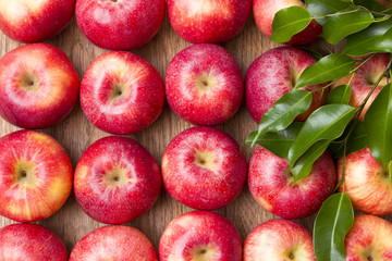 Many red apples with leaves on a wooden background.