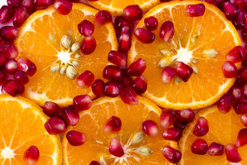 Macro peeled ripe pomegranate fruit with many slices of orange f