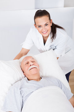 Happy Doctor With Senior Man Lying In Bed