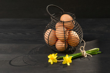 Yellow narcissus on wooden table next to egg basket.