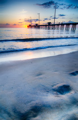 The rising sun peeks through clouds and is reflected in waves by