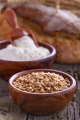 Bowl of wheat and flour withl the bread on a wooden table