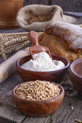Bowl of wheat and flour withl the bread on a wooden table