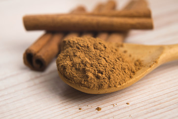 Cinnamon, whole sticks behind wooden spoon with a heap of powder