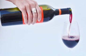 A woman's hand holding a bottle pouring red wine.