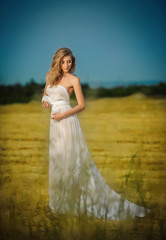 Fototapeta na wymiar Young woman in white long dress standing on a wheat field 