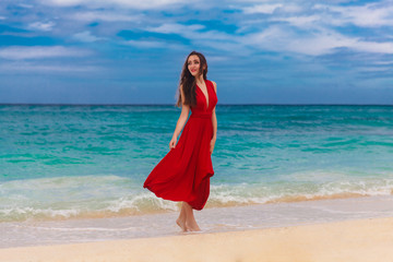Fototapeta na wymiar Smiling beautiful woman in a red dress standing on the sea coas
