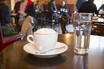 cup of cappuccino  and glass of water on wooden table