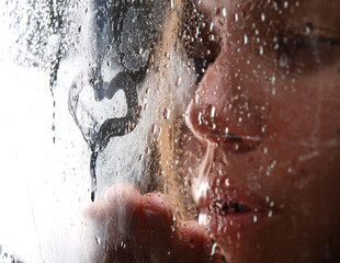A girl slooking through the wet glass