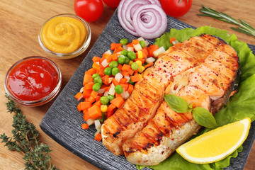 Tasty grilled salmon with vegetables, on wooden table