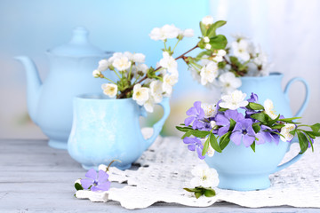 Beautiful spring flowers in cups on wooden table