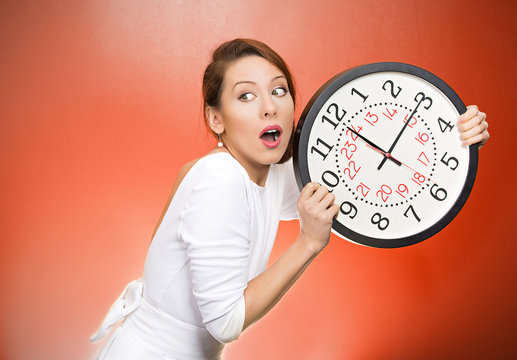 Running out of time. Girl holding wall clock on red background 