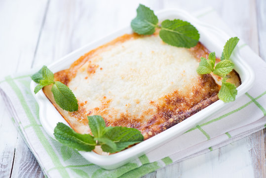 Vegetable lasagna with mint leaves over white wooden background