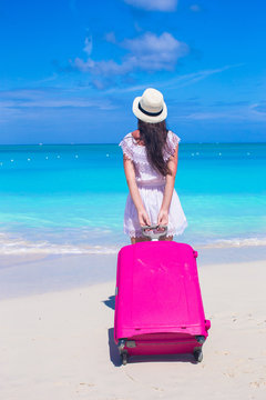 Back view of young beautiful woman with large suitcase on