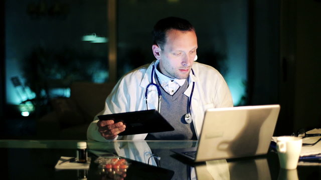 Young Doctor Working On Laptop And Tablet Computer Late At Night