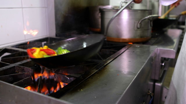 Chef frying vegetables in a wok and adding ladle of water