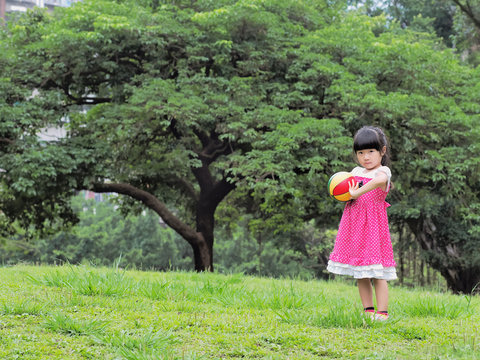 The girl playing the ball on the grass in the park.