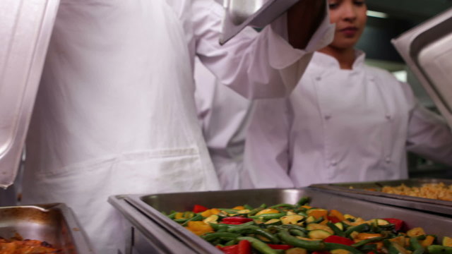 Row of chefs lifting lid off serving trays