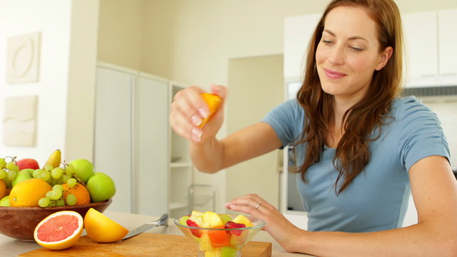 Pretty woman preparing a fruit salad smiling at camera