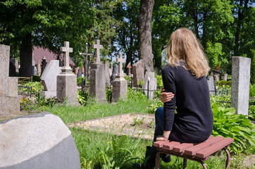 Sorrow woman near father husband tomb in cemetery