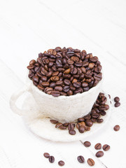 cup full of coffee beans on a white wooden background