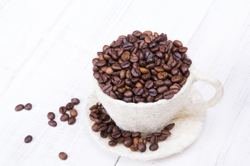 cup full of coffee beans on a white wooden background