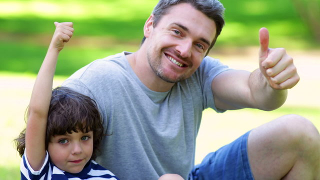 Father sitting with little son in the park showing thumbs up