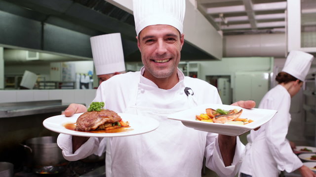 Smiling handsome chef showing two dishes to camera