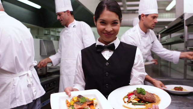 Smiling waitress showing two dishes to camera