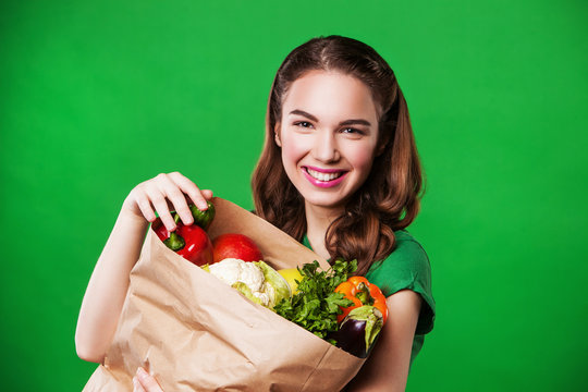 Happy healthy woman with a paper bag of vegetables. on green