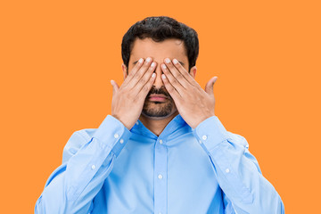 See no evil concept. Man covering eyes on orange background 