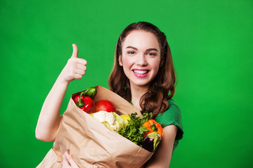 Young smiling woman with a paper bag of vegetables. on green